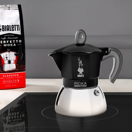 Bialetti Moka Induktion 2 kopper sort placeret på induktionskomfur ved siden af kaffepose